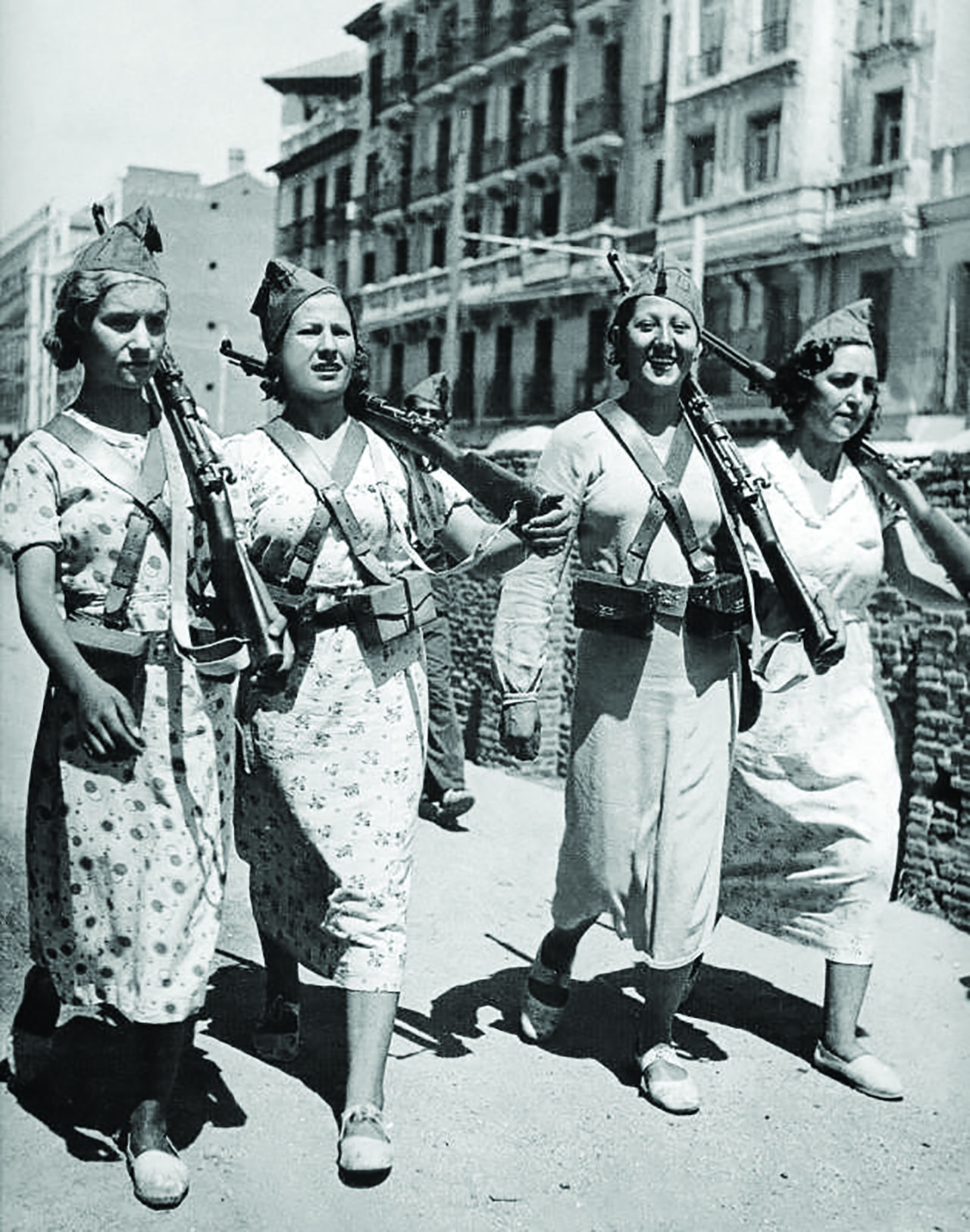 Four militia women in dresses walking with machine guns over shoulders