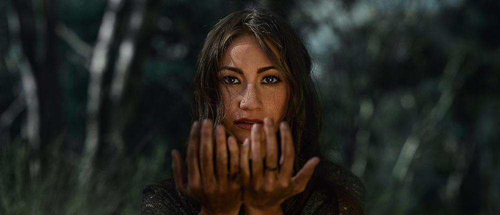 A close up of a womens face with her hands reaching out