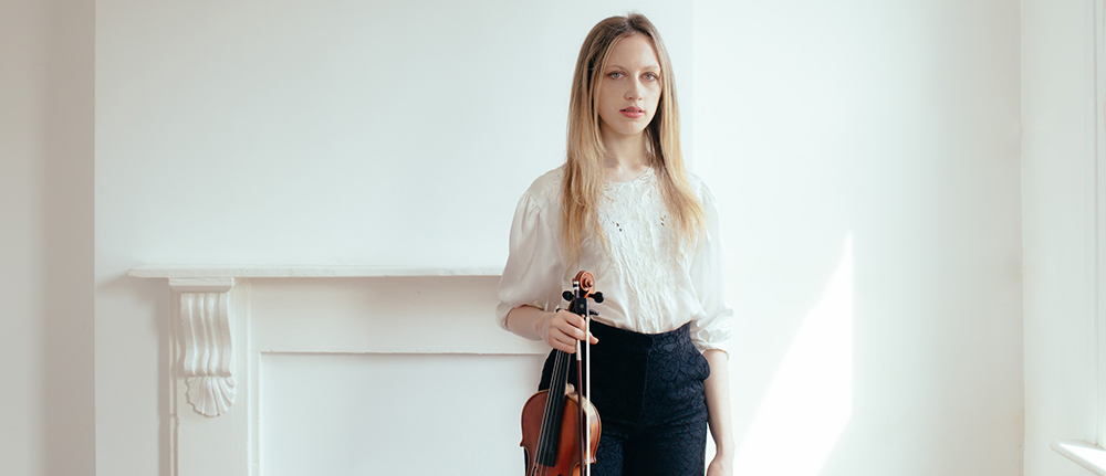 standing woman with long blonde hair holding a violin