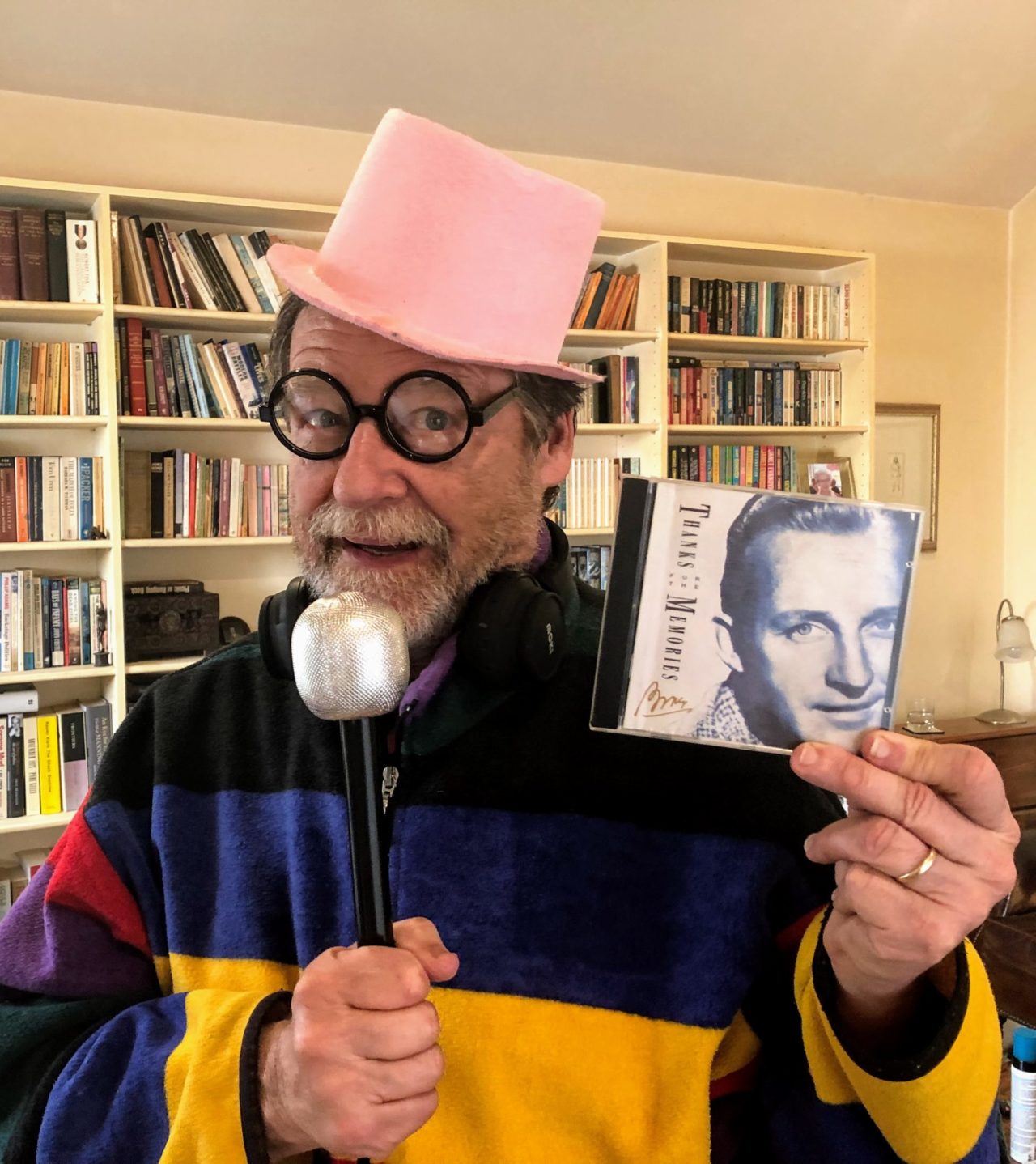 A man in a pink top hat with a fake microphone holding a Bing Crosby CD