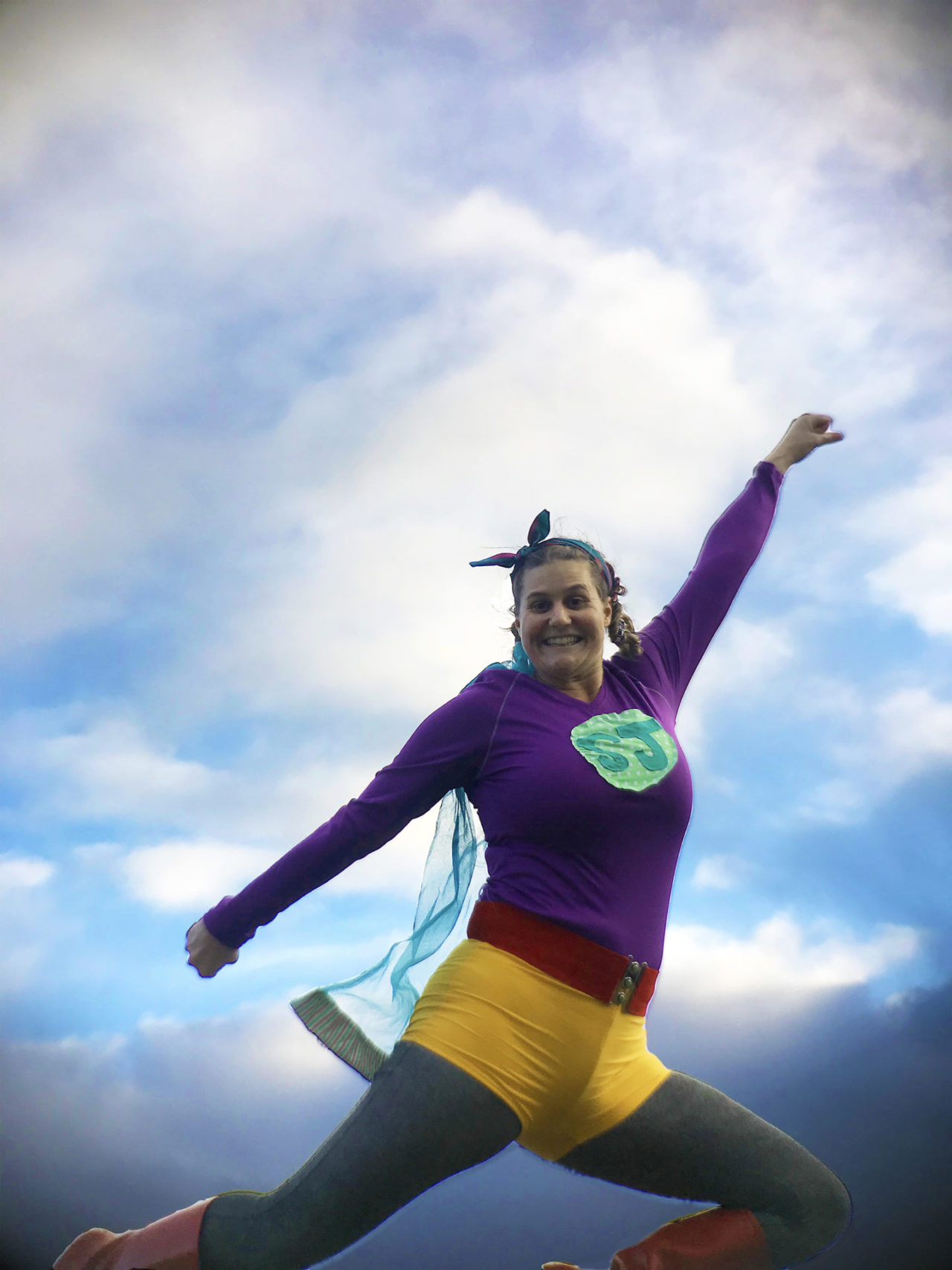 A woman in a super hero costume holding a strong pose with a big smile on her face