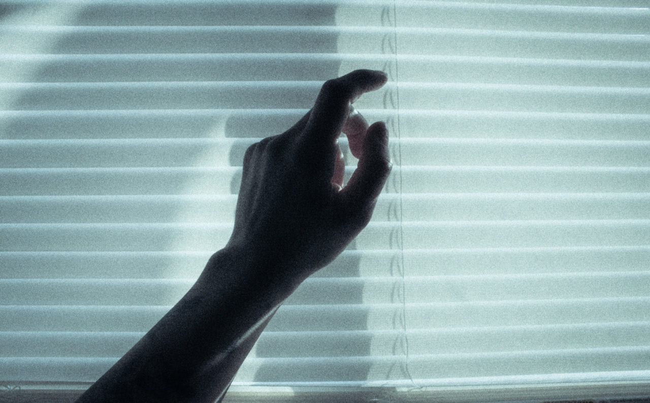 A hand touches closed blinds