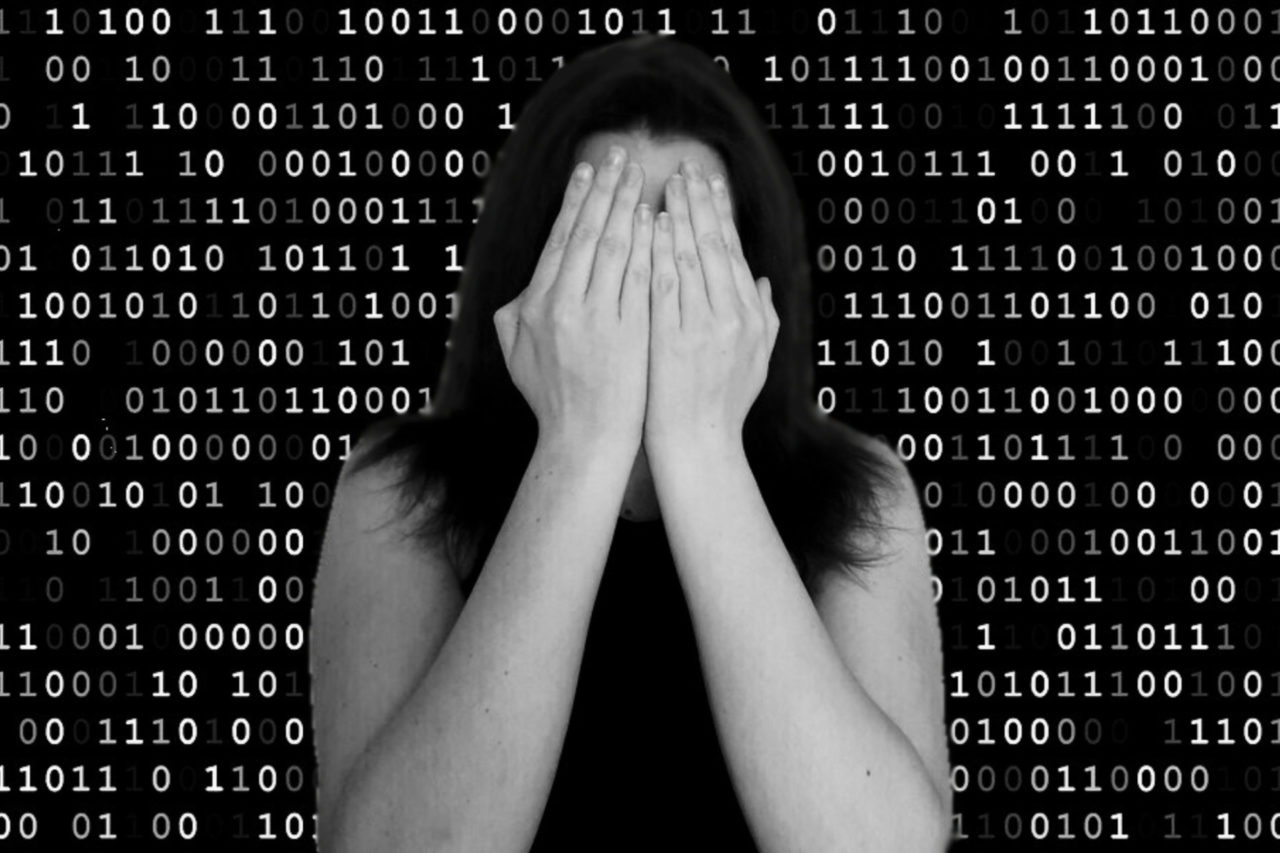 Black and white image of a pale, dark haired woman covering her face with her hands, against a backdrop of binary code.