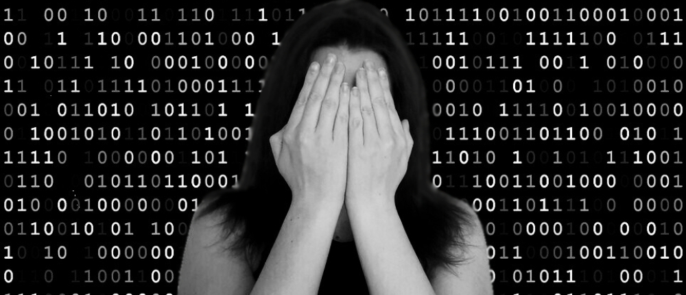 Black and white image of a pale, dark haired woman covering her face with her hands, against a backdrop of binary code.