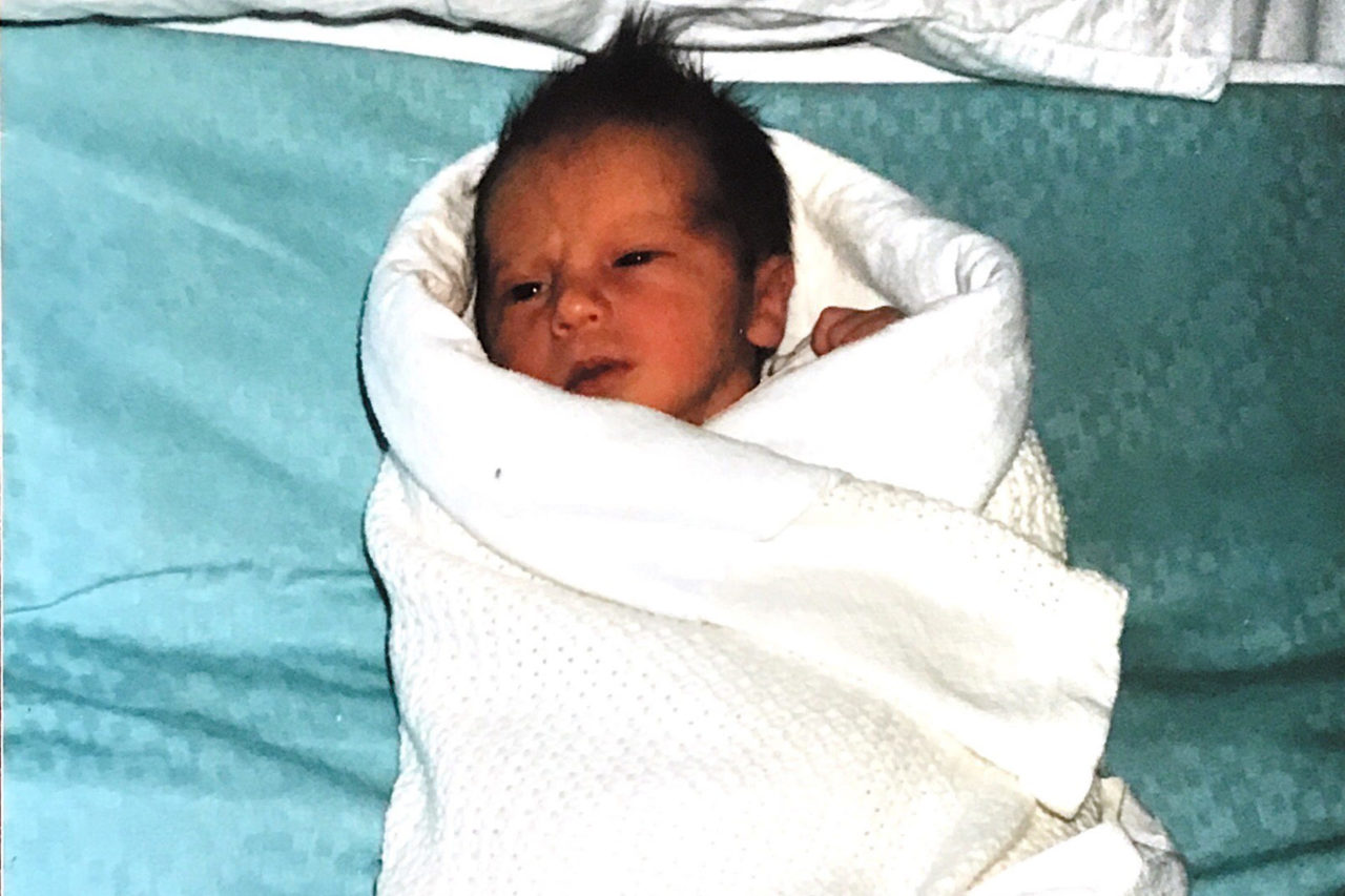 A newborn baby wrapped in a white cloth, lying on a blue blanket.