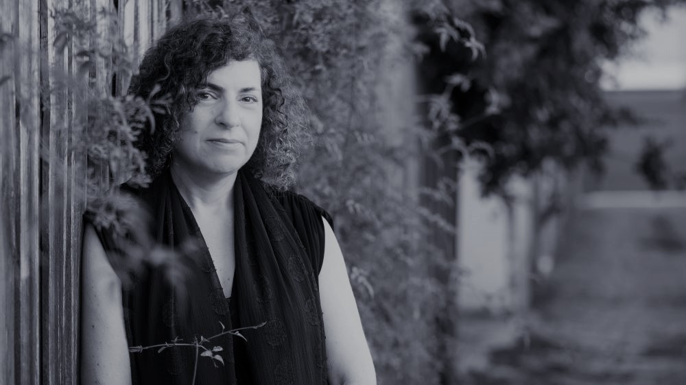 A black and white photo os a woman with short curly hair leaning against a fence