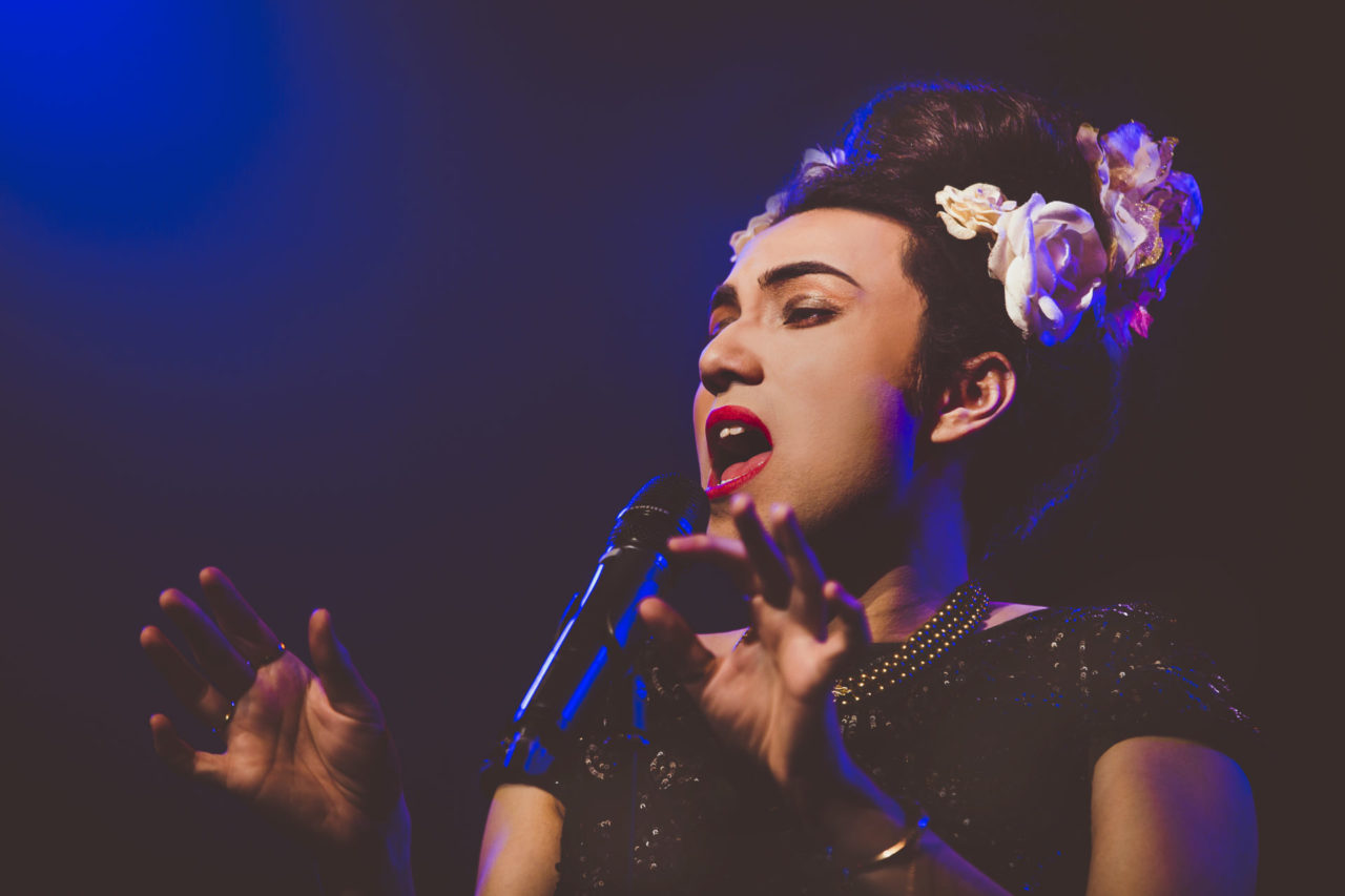 A singer singing into a microphone with blue light across her face.