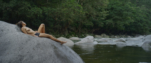 A person lying down on the rocks of a river