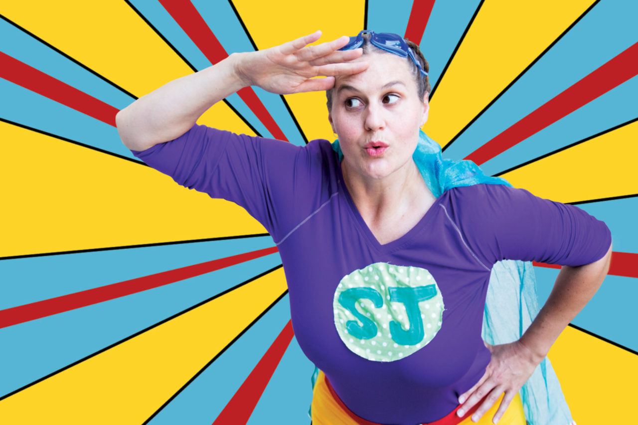 Super Jenny poses on a bright pop art style background of yellow, blue and red.