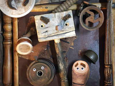 Amongst some salvaged wood, a trio of wooden puppet characters look nervously at each other.