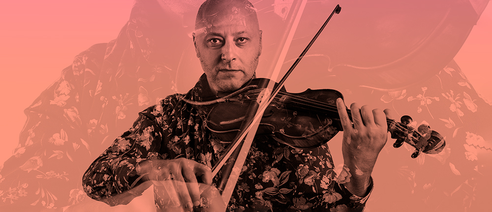 A man in a floral shirt plays violin, looking intensely into the camera.