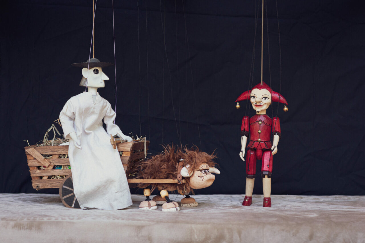 a peasant stands next to a cart driven by an ox. He looks across to a young man wearing a red tunic and jester’s hat. Image: Kasia Pudlo