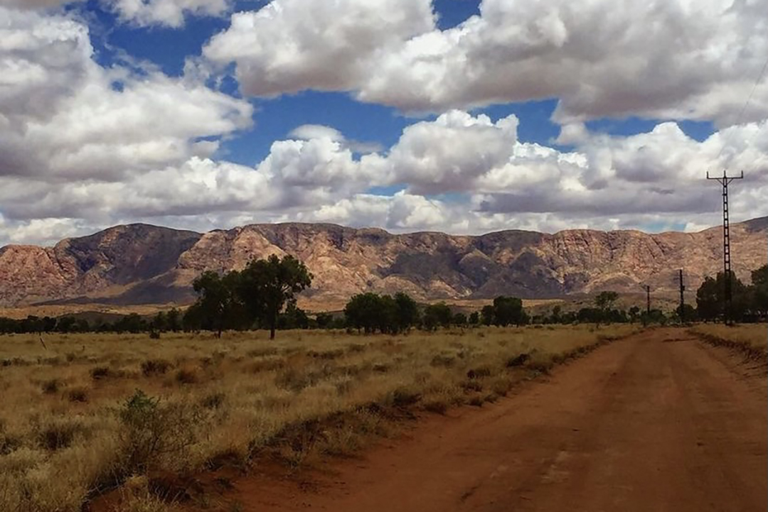 A red dirt road, a mountain and blue sky with clouds