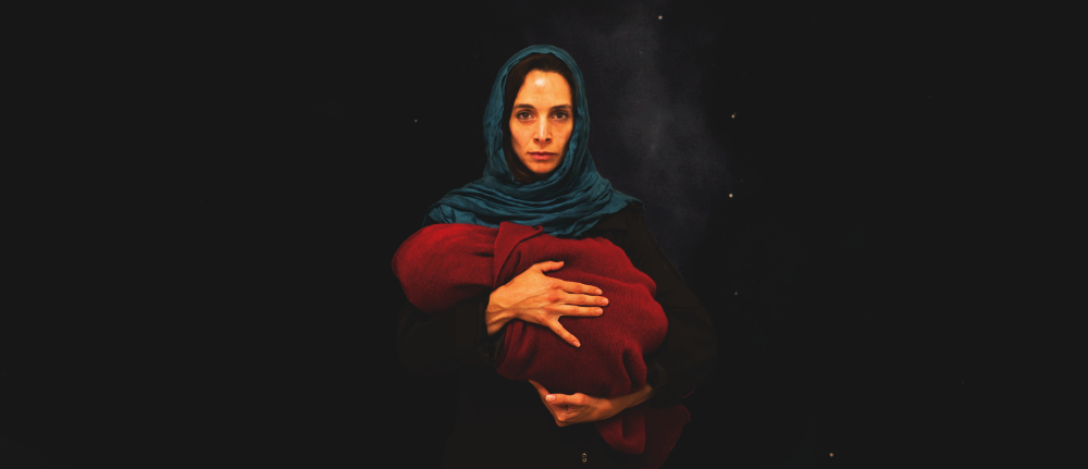 A woman in a blue scarf holds a baby wrapped in a red blanket, a dark night sky behind them.