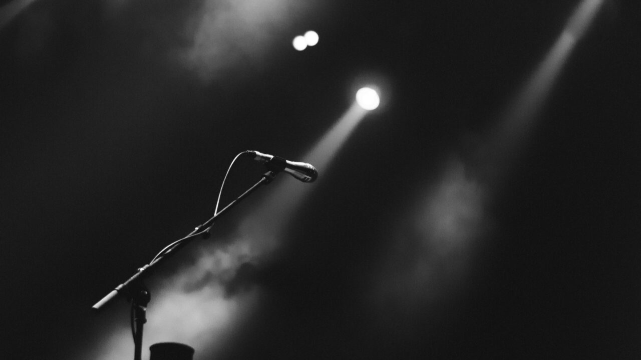 A black and white image of a microphone on a stage with misty stage lighting