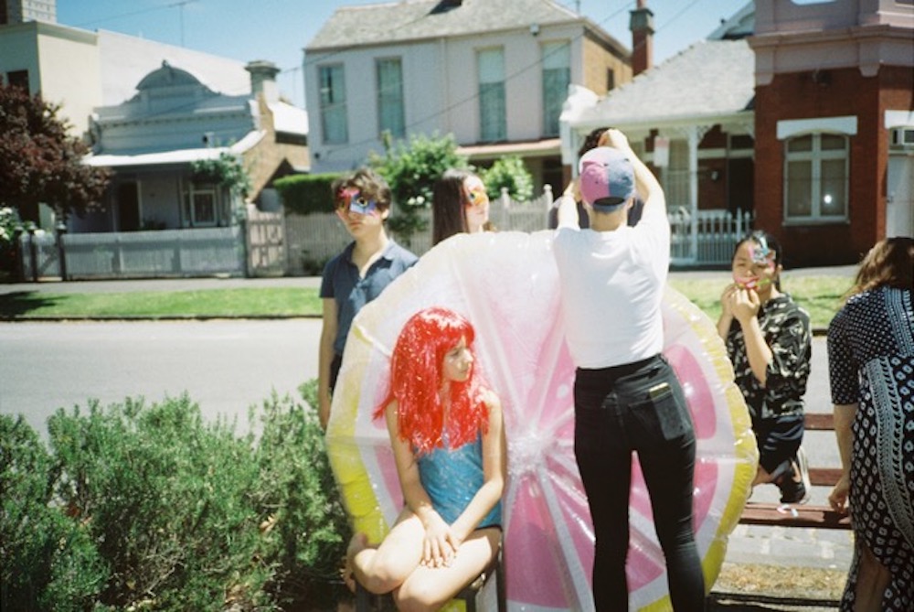 A group of teenagers sitting and standing around an inflated grapefruit in front of a road