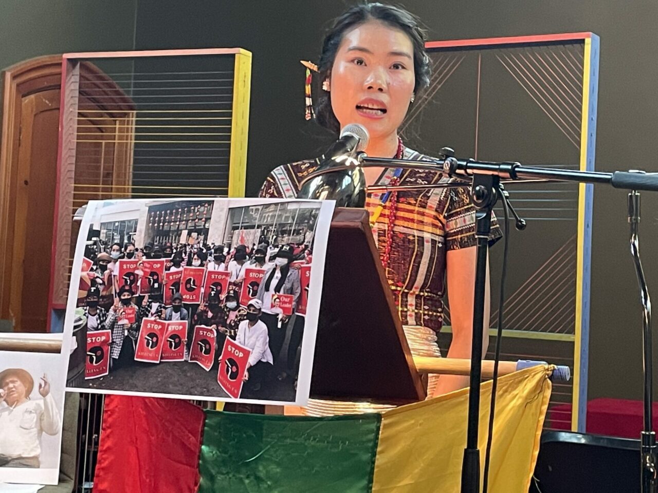 A woman wearing colourful traditional Burmese dress is reading a text from a lectern