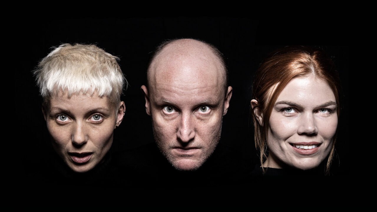 Three faces, floating in space, stare out from the world of the play