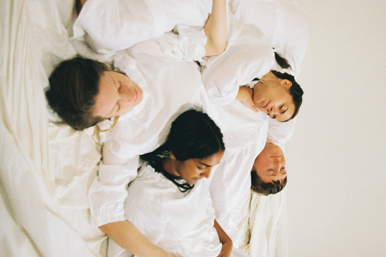 Four people in white clothes are laying down, with their bodies overlapping. They seem to be sleeping.