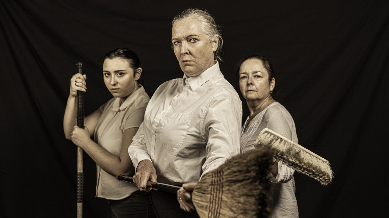 Three women of different ages holding brooms in a defiant manner.