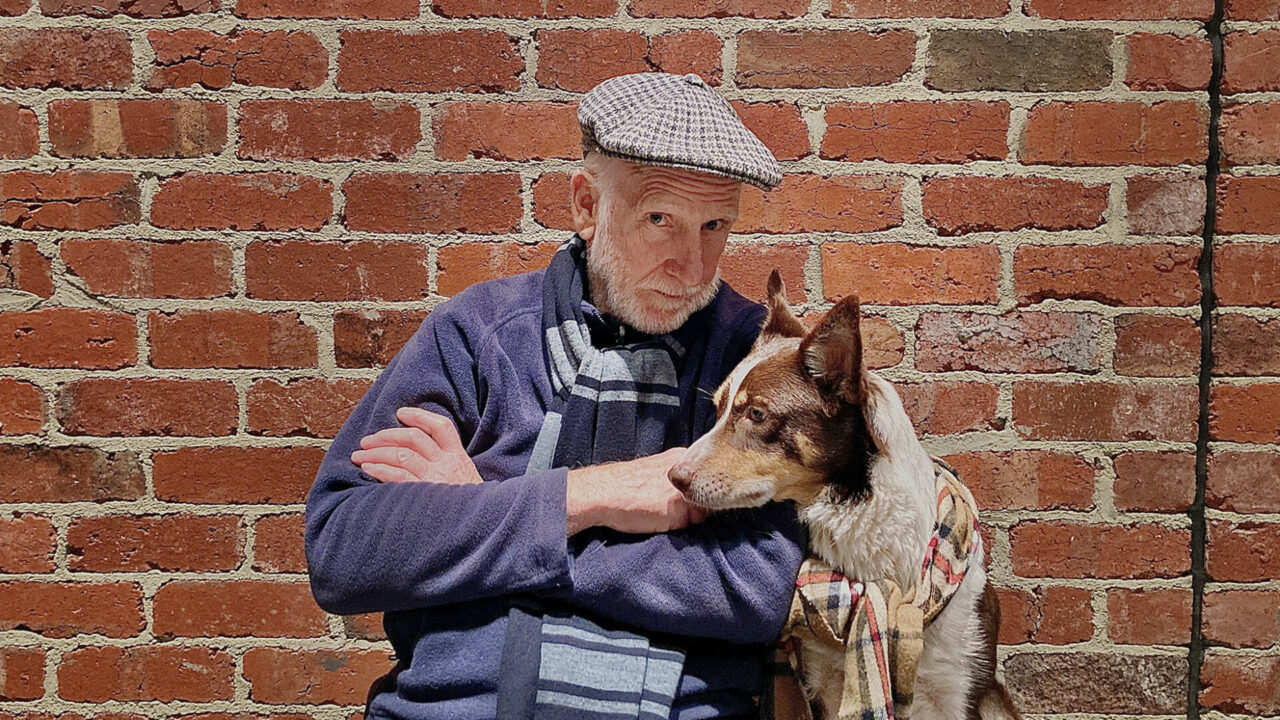 In the sunshine a man and a dog sit together against a brick wall