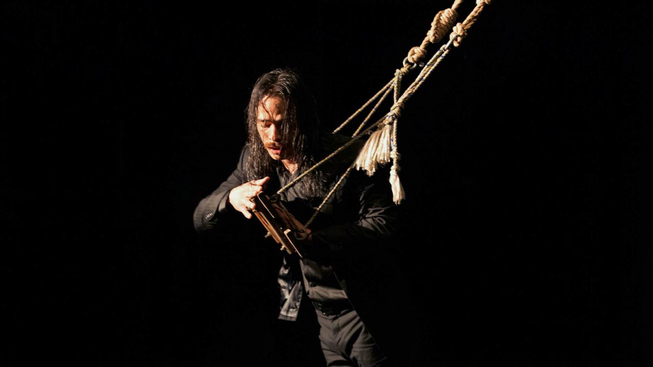 A man in a wet black suit balances on an old wooden swing. He