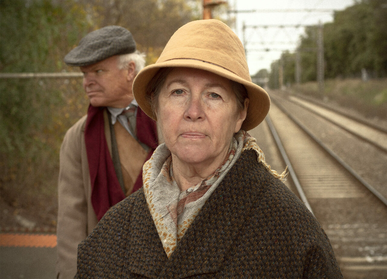An older woman staring down the camera from a train platform