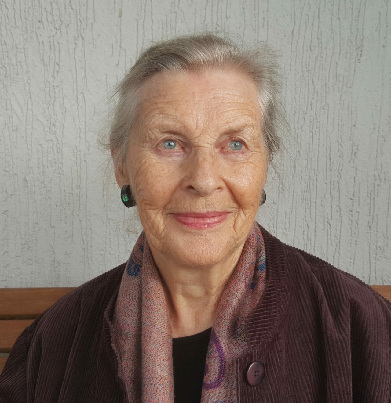 An elderly woman with bright blue eyes and white hair is looking into the distance with a slight smile.