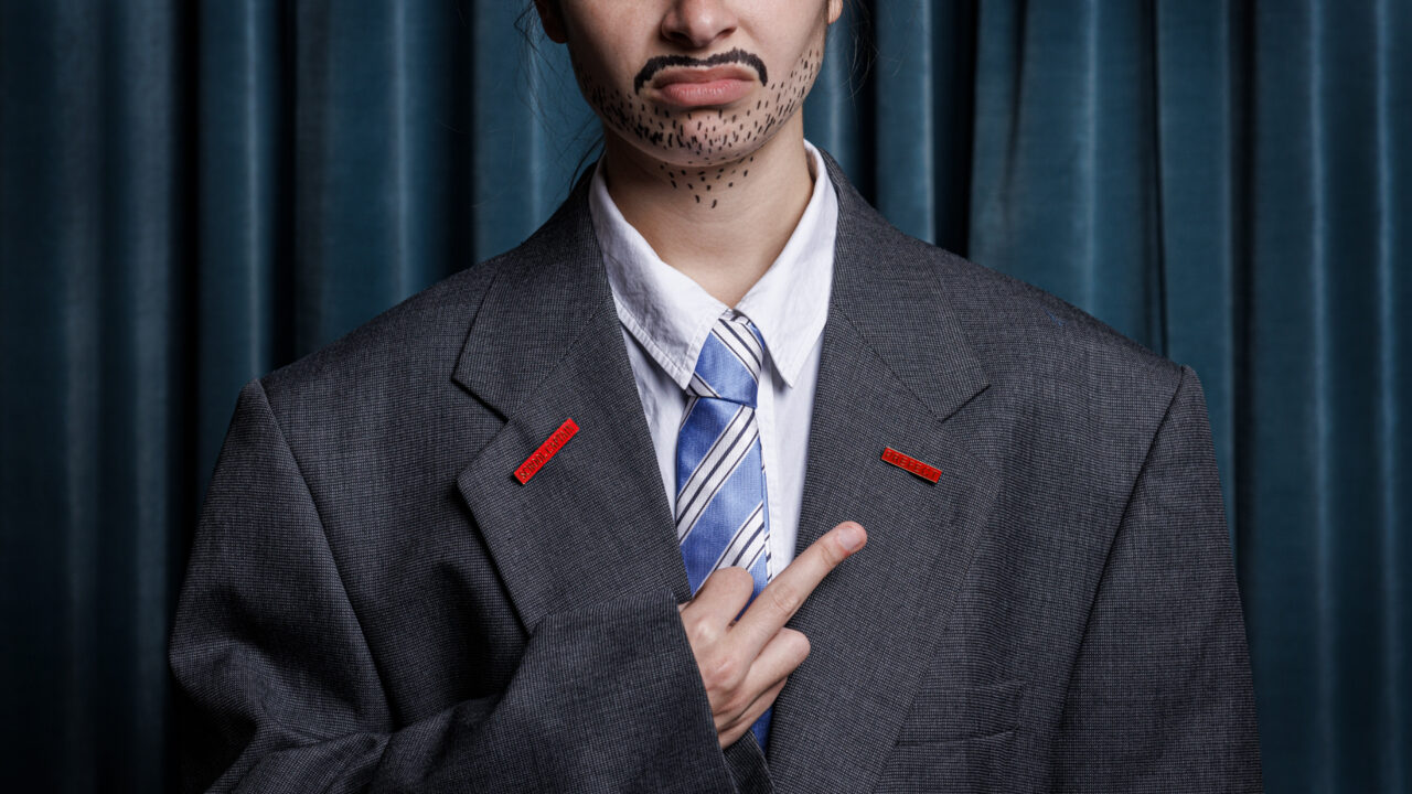 A person stands in front of a curtain, posing for a school photo with their rude finger out.