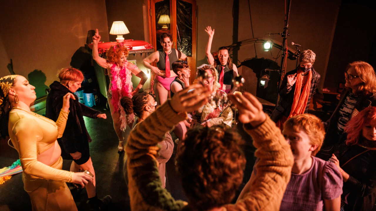 A group of people dance joyously on stage after a performance.